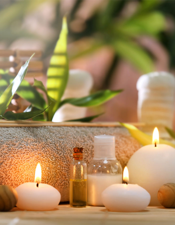 candles and bottles of spa oil sitting on a table in front of green plants and a plush cushion